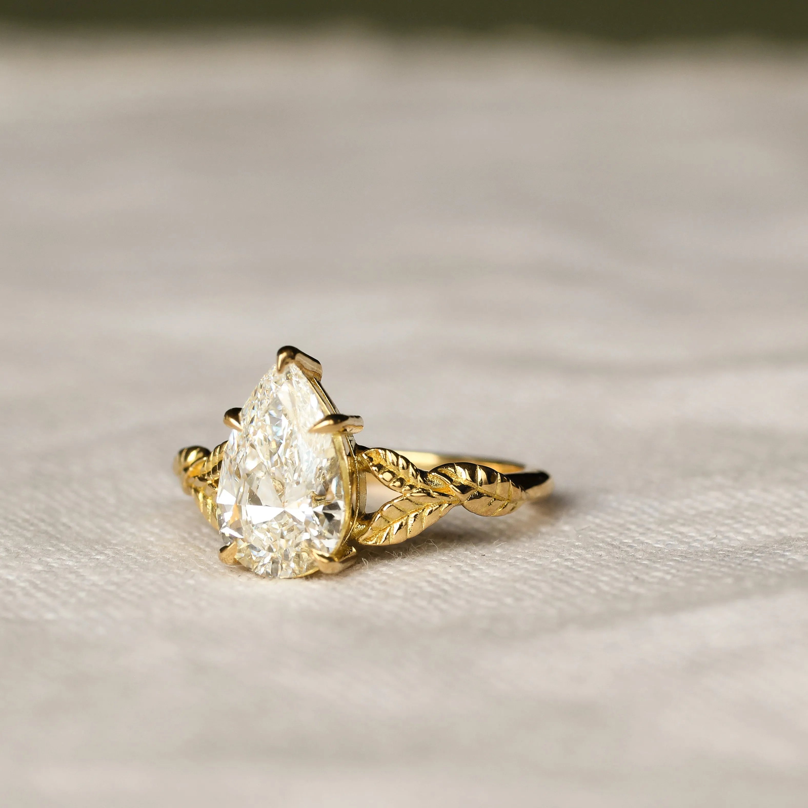 engagement ring with leaves on band and pear diamond on a neutral fabric