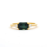 Gold engagement ring with a east-west emerald-cut blue green parti sapphire and diamonds on a white background