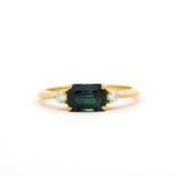 Gold engagement ring with a east-west emerald-cut blue green parti sapphire and diamonds on a white background