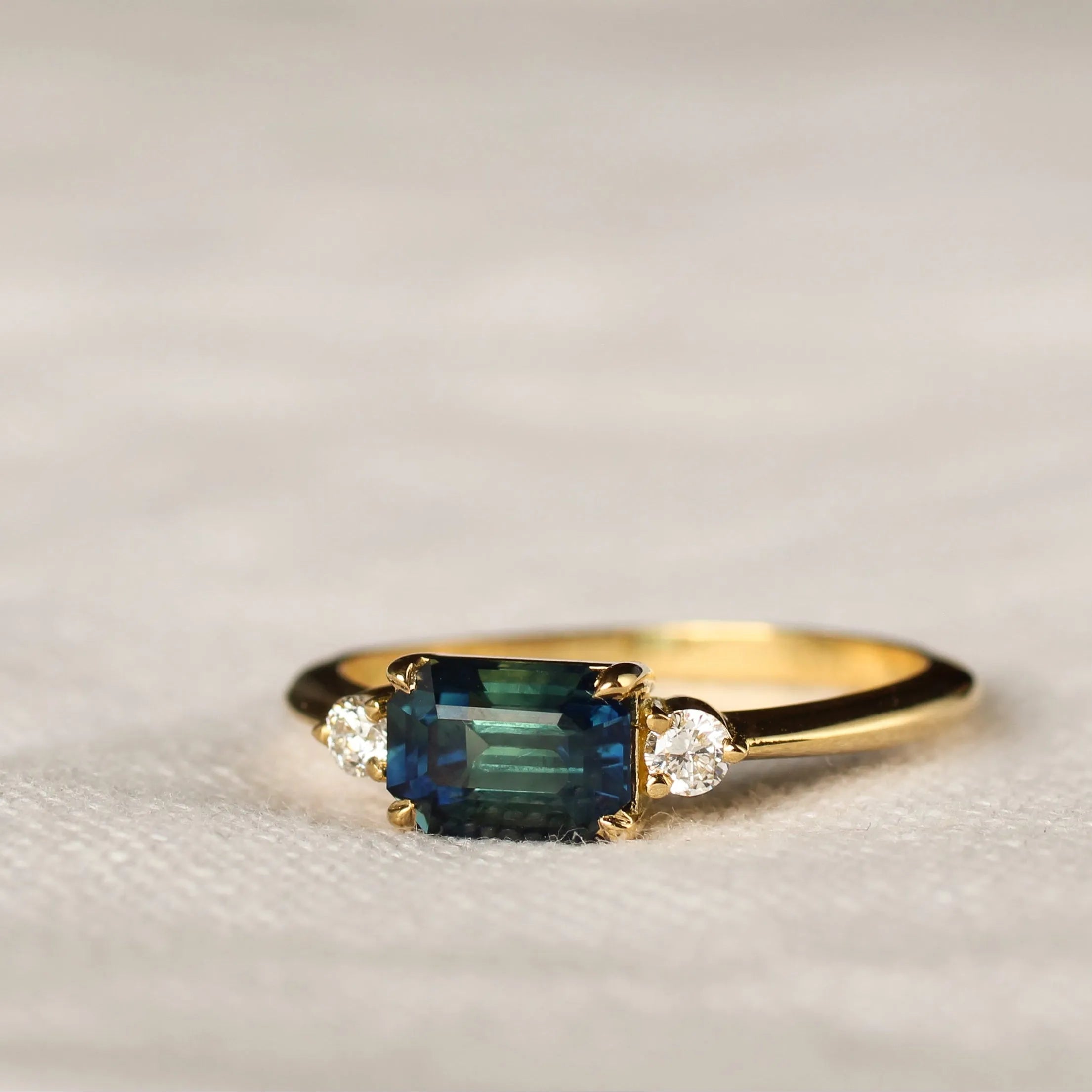 gold ring with bi colour parti sapphire in east-west setting with round diamonds on a beige blurred surface
