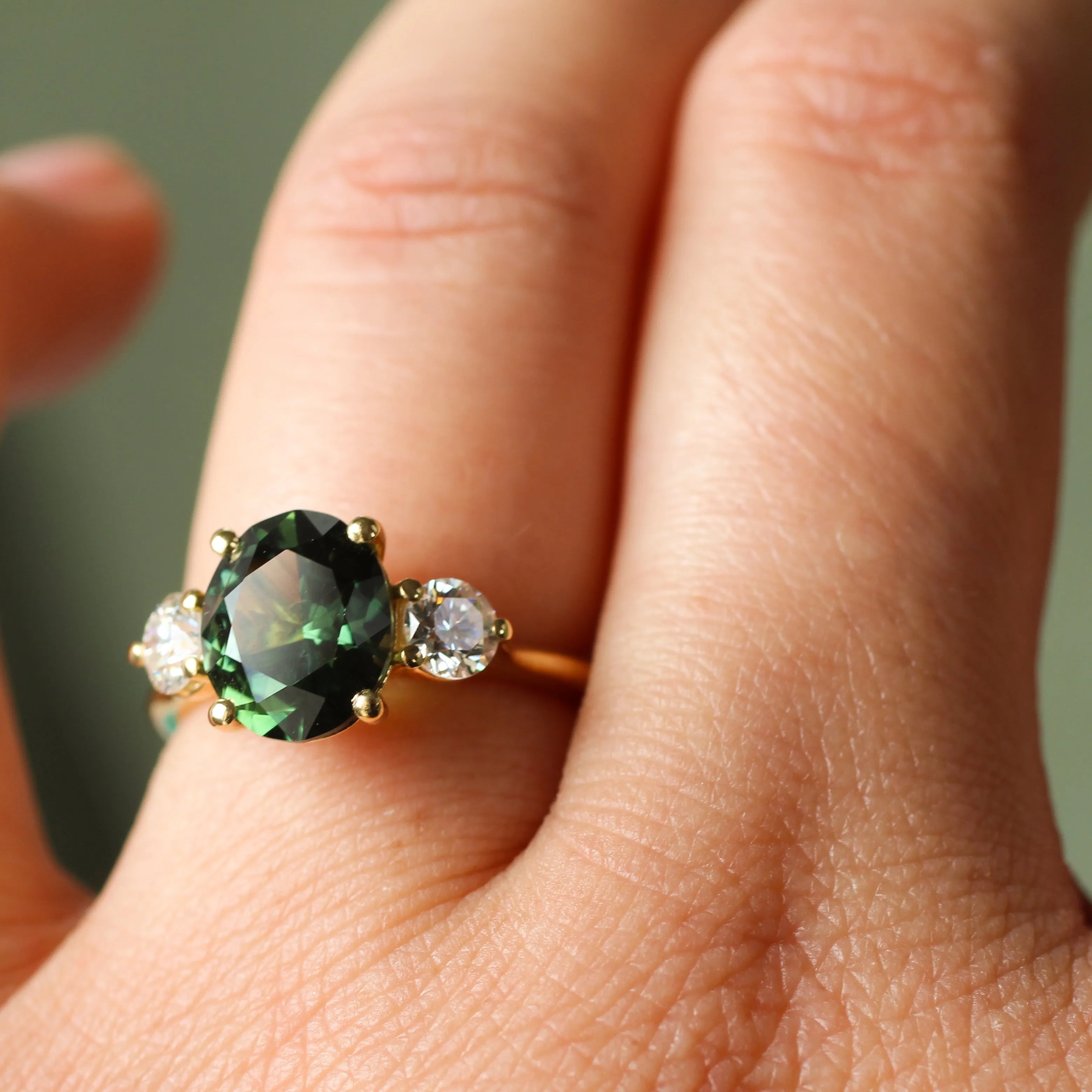 Close-up of a hand wearing a large green sapphire engagement ring with smaller diamonds.