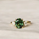 Gold trilogy ring with a large green sapphire and large 4mm round diamonds on a light background