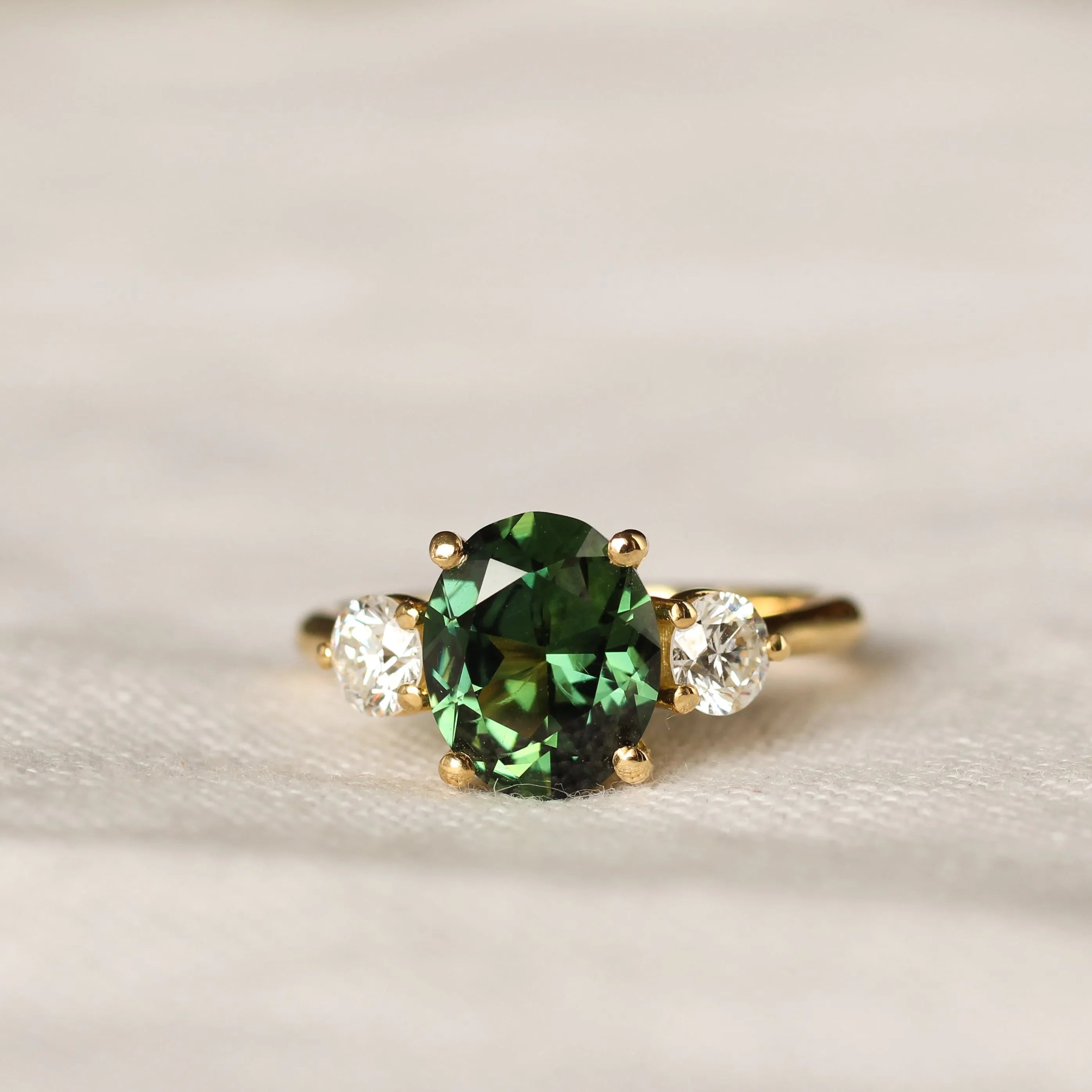 Gold trilogy ring with a large green sapphire and large 4mm round diamonds on a light background