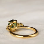 back view of large green sapphire engagement ring with high setting with a green gemstone on a light fabric background