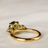 back view of large green sapphire engagement ring with high setting with a green gemstone on a light fabric background