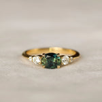 bi colour sapphire engagement ring with east-west oval sapphire with blue and green colours, round diamonds on a neutral surface