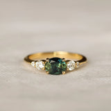 bi colour sapphire engagement ring with east-west oval sapphire with blue and green colours, round diamonds on a neutral surface