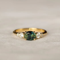 bi colour sapphire engagement ring with east-west oval sapphire with blue and green colours, round diamonds on a neutral surface