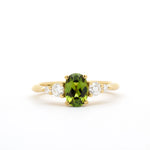gold engagement ring with a green oval sapphire and four diamonds in tapered composition on a white background
