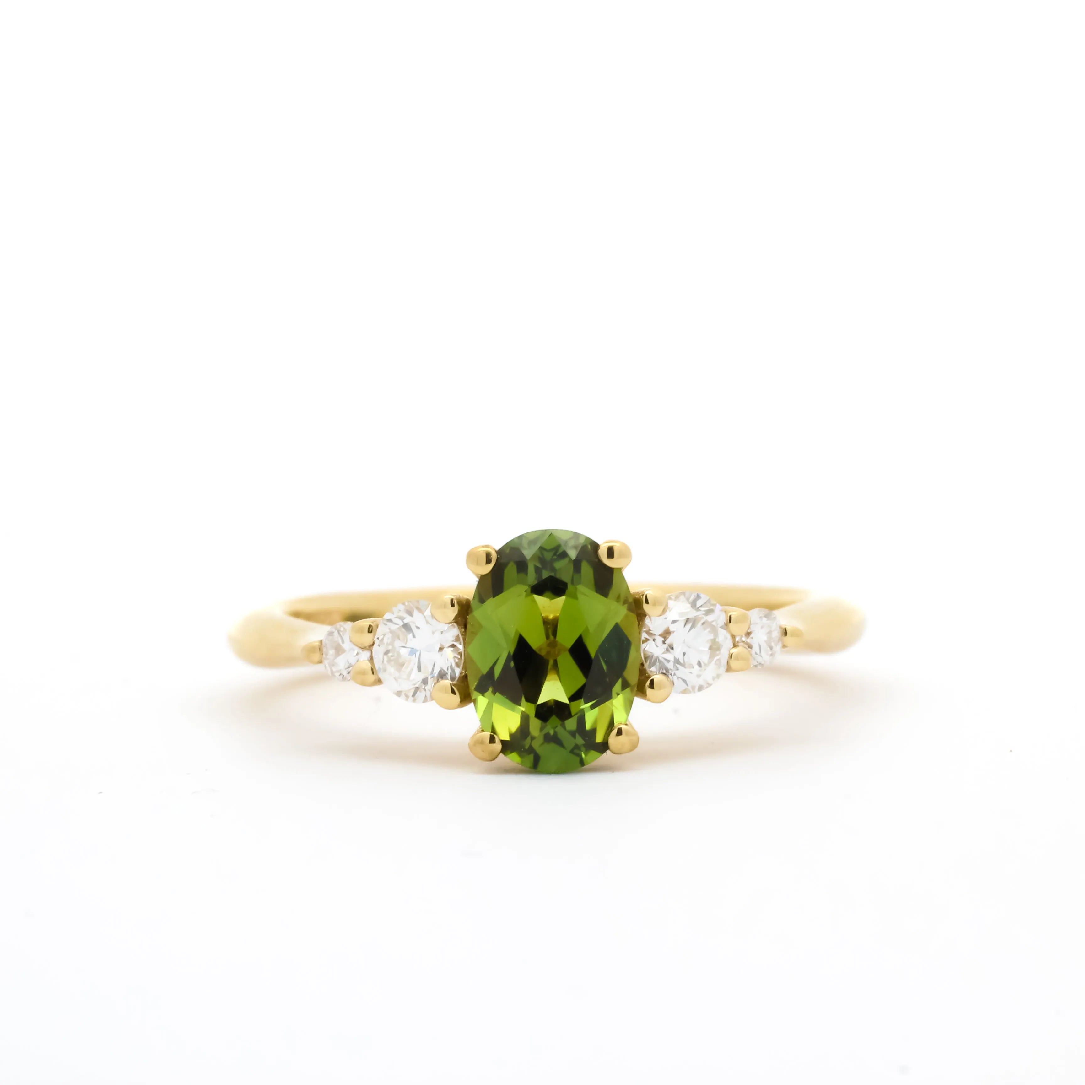 gold engagement ring with a green oval sapphire and four diamonds in tapered composition on a white background