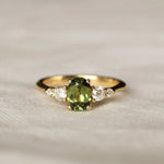 Gold ring with a green gemstone and smaller diamonds on a soft fabric background