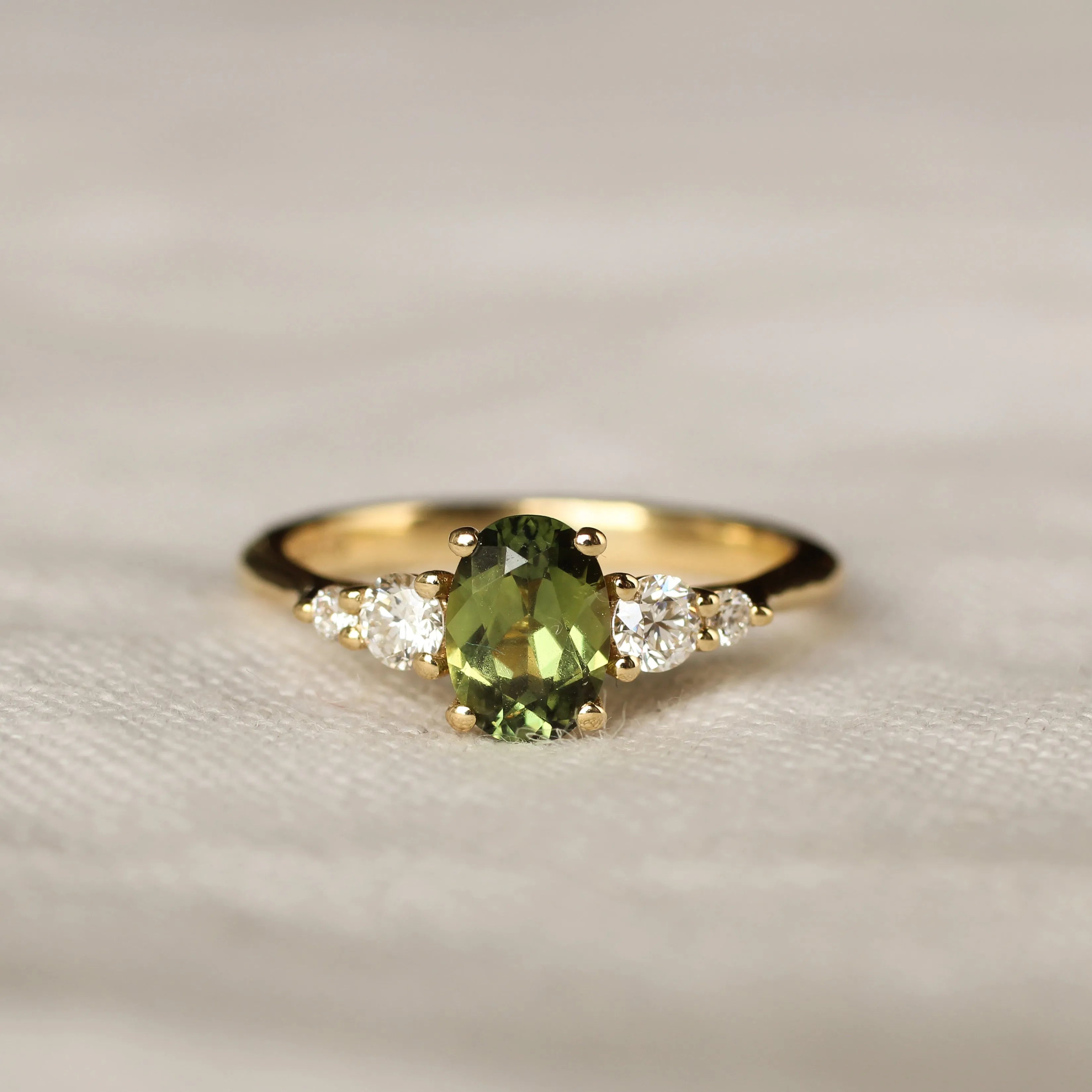 Gold ring with a green gemstone and smaller diamonds on a soft fabric background