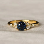 royal blue sapphire engagement ring with round gemstone and scattered diamonds on a textured beige background