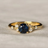 royal blue sapphire engagement ring with round gemstone and scattered diamonds on a textured beige background