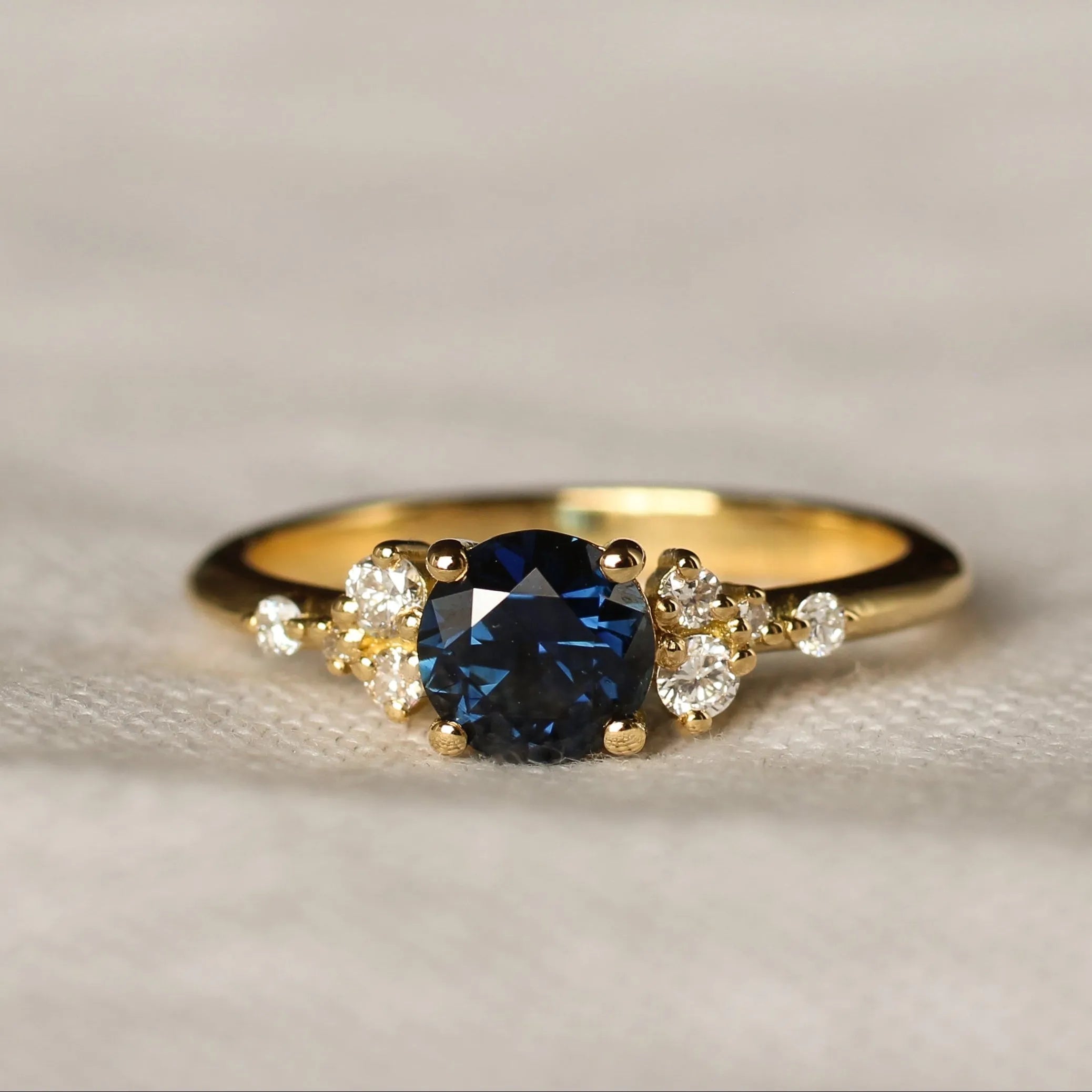 royal blue sapphire engagement ring with round gemstone and scattered diamonds on a textured beige background
