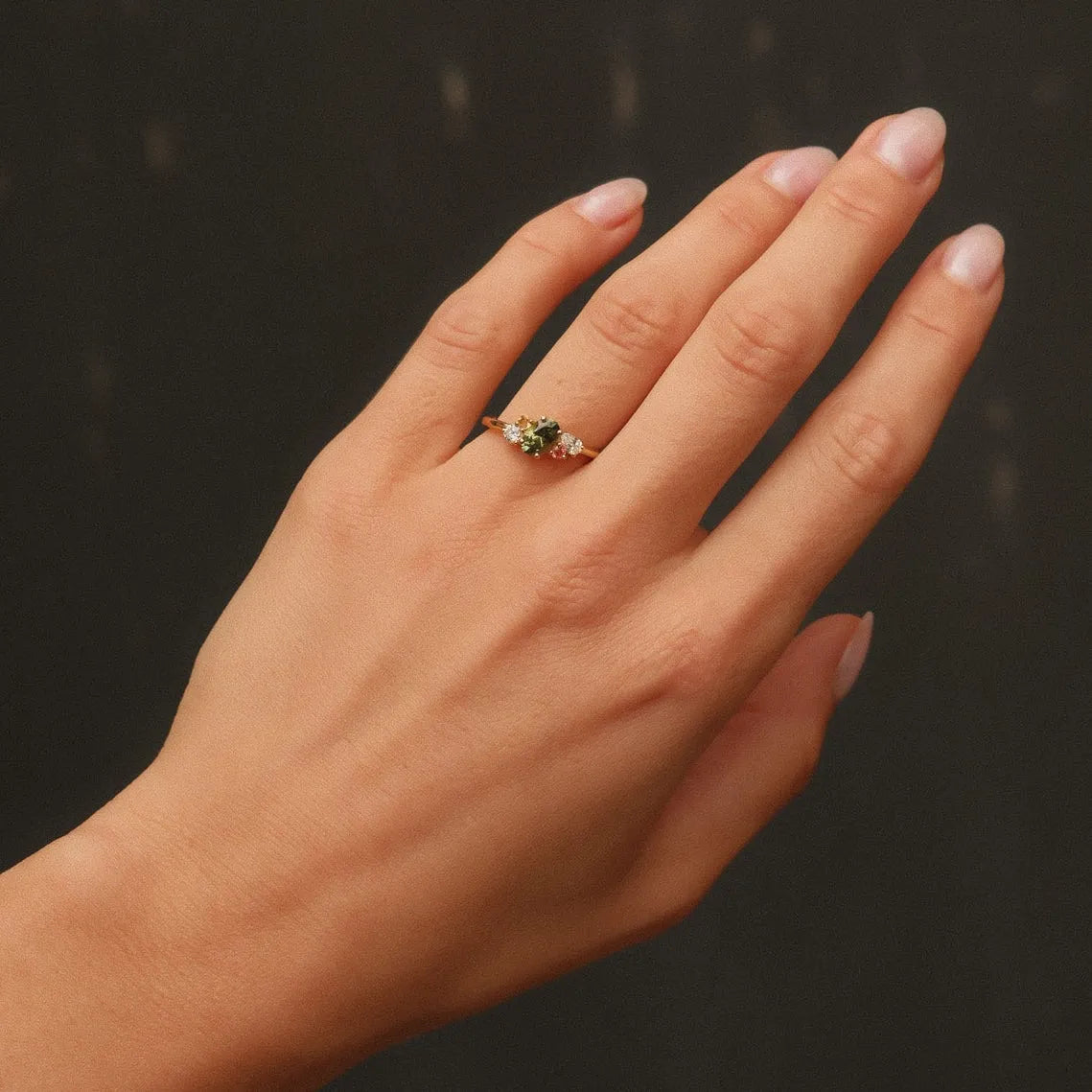 Hand wearing a ring with colourful gemstones against a dark background
