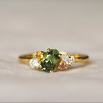 colourful engagement ring with green, pink and yellow sapphires with diamonds on a light background