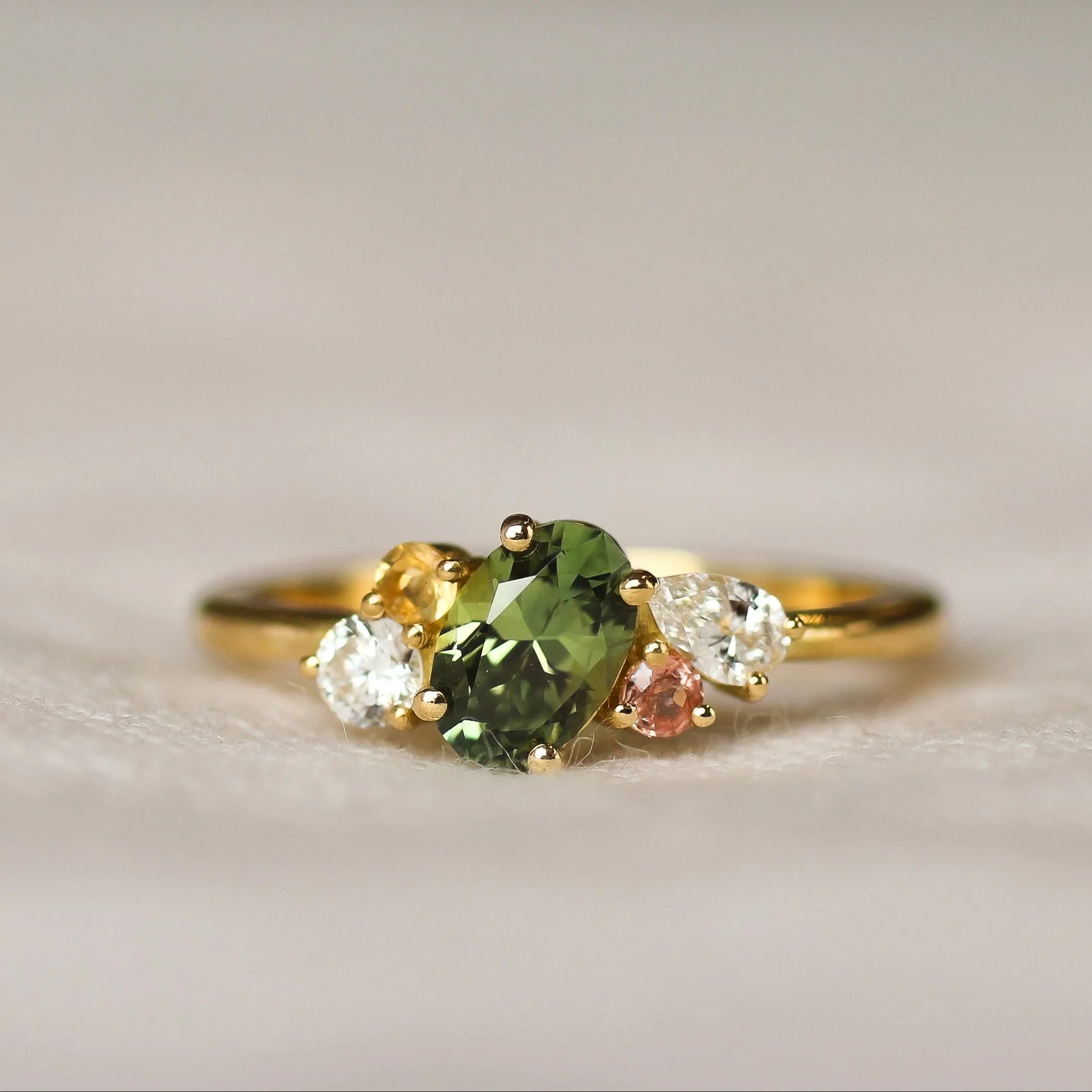 colourful engagement ring with green, pink and yellow sapphires with diamonds on a light background