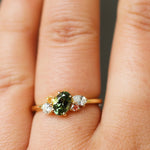 close up of hand wearing a green sapphire engagement ring with yellow and pink sapphires and diamonds