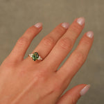 Hand wearing a ring with a green gemstone on a neutral background