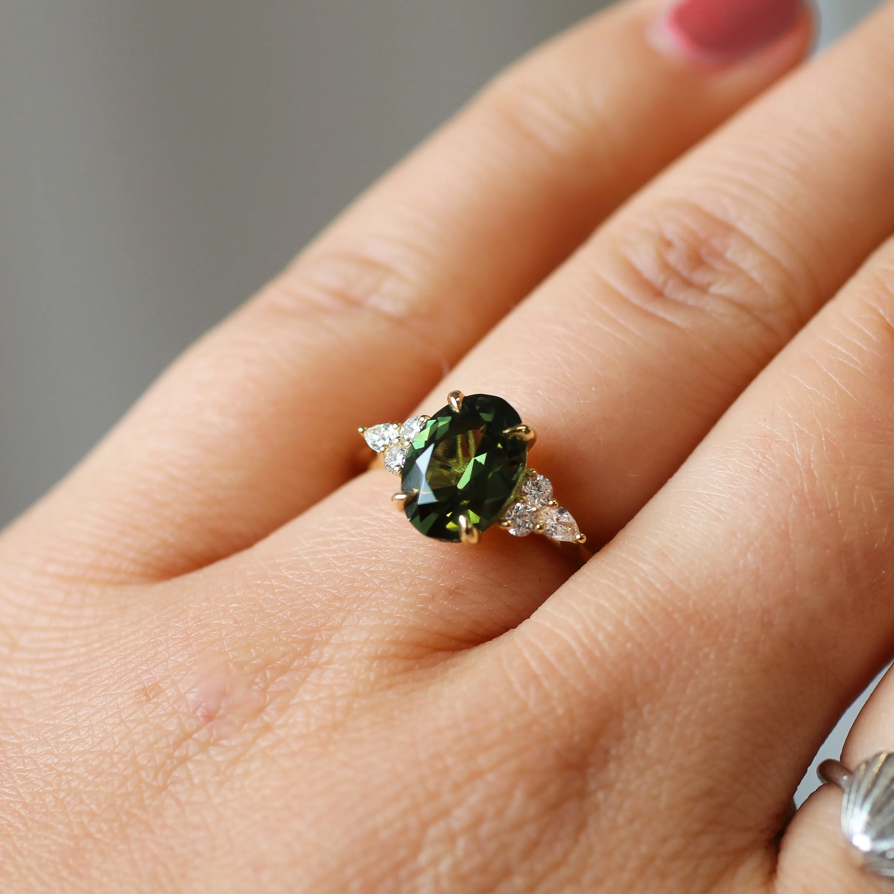 close up of hand wearing Large Green Sapphire Engagement Ring with Pear & Round Diamond Cluster