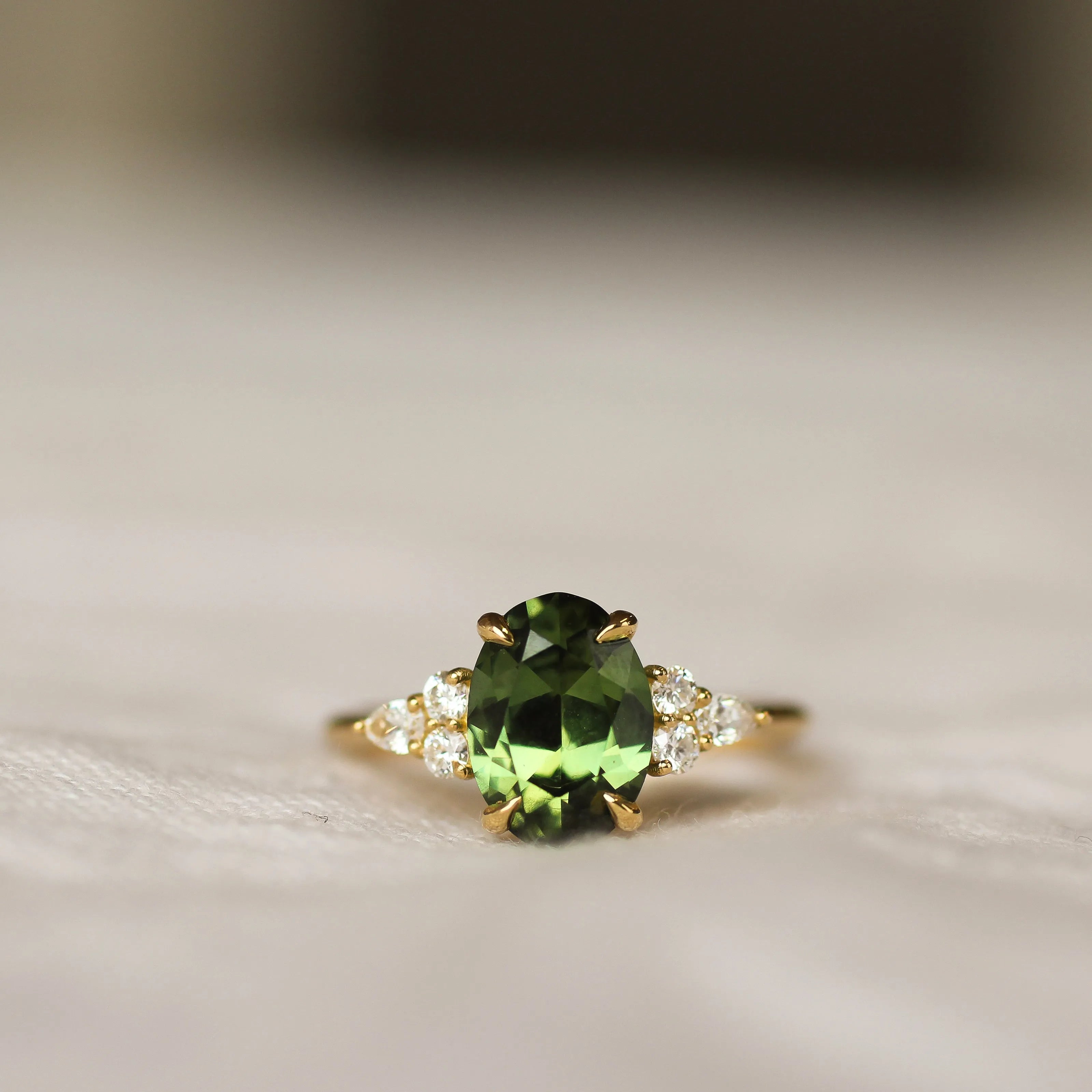 Ring with a large green gemstone and gold setting on a neutral background