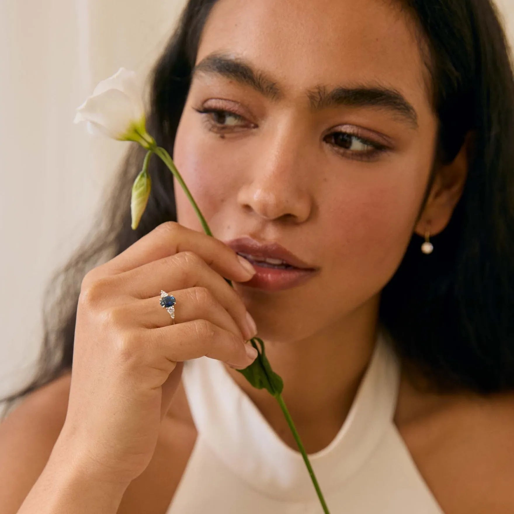 woman holding a white flower wearing a blue sapphire engagement ring