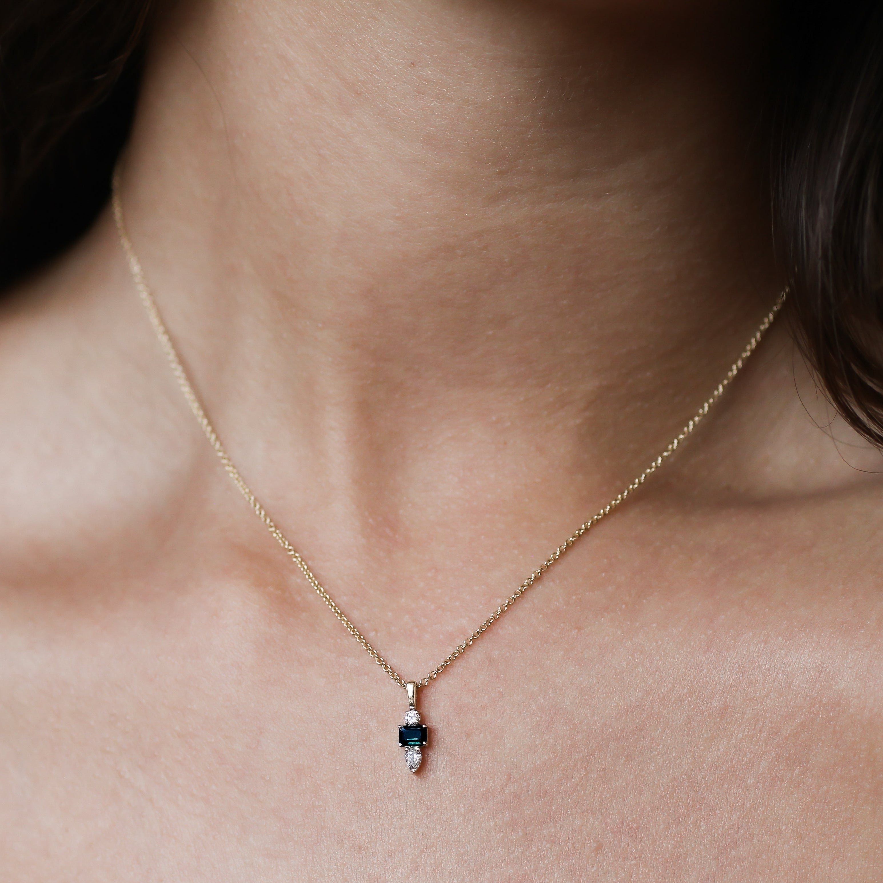 close up of a dainty dark blue sapphire and diamond necklace shown worn on a models neck
