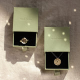 Two pieces of gold moon jewellery in open green boxes on a textured surface