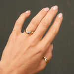 Hand wearing chunky gold curved wedding ring on a dark background