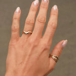 Hand wearing a curved chunky gold wedding ring and gold thumb rings with a neutral background