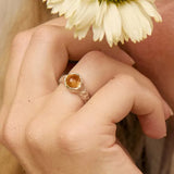 close up of a hand holding a flower wearing a silver organic ring with round orange citrine gemstone
