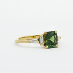 Gold ring with a green cushion sapphire and tapered baguette diamonds on a white background
