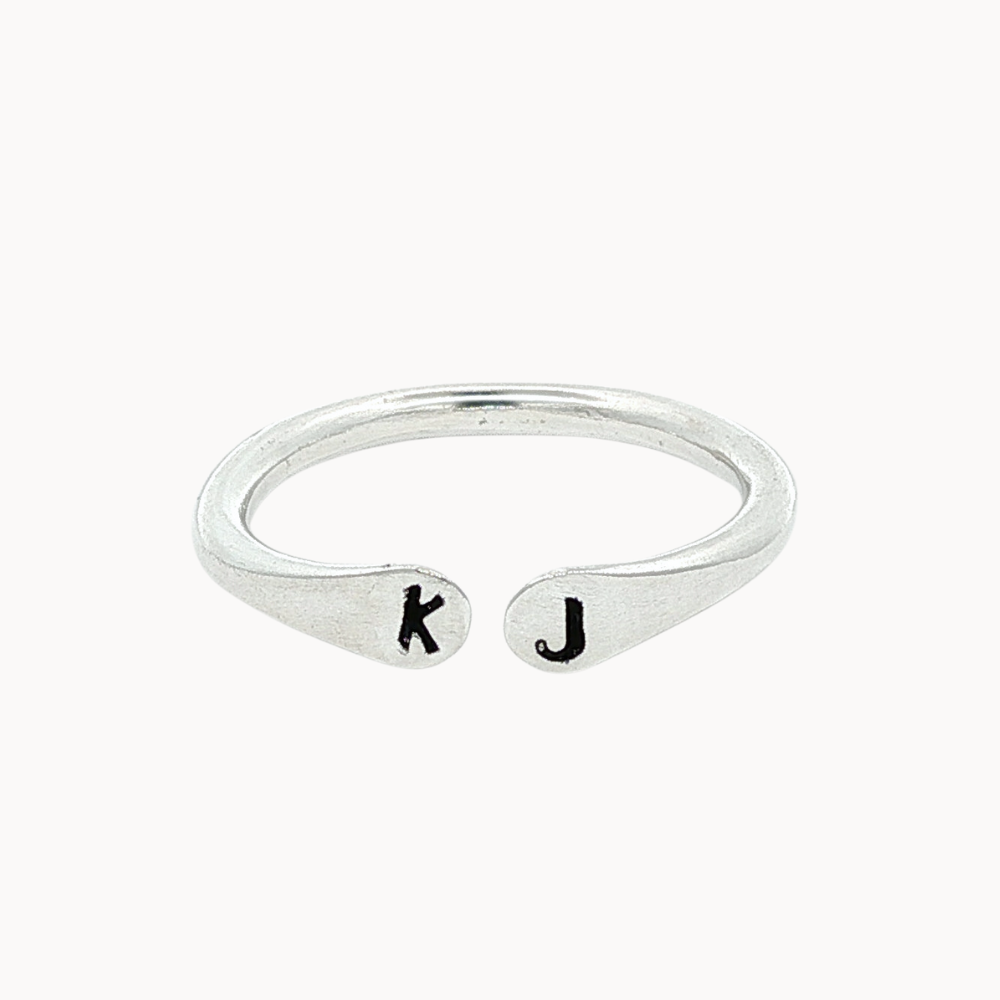 silver open ring with 'k' and 'j' stamped initials on a white background