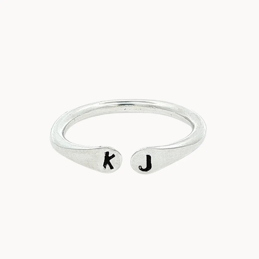 silver open ring with 'k' and 'j' stamped initials on a white background