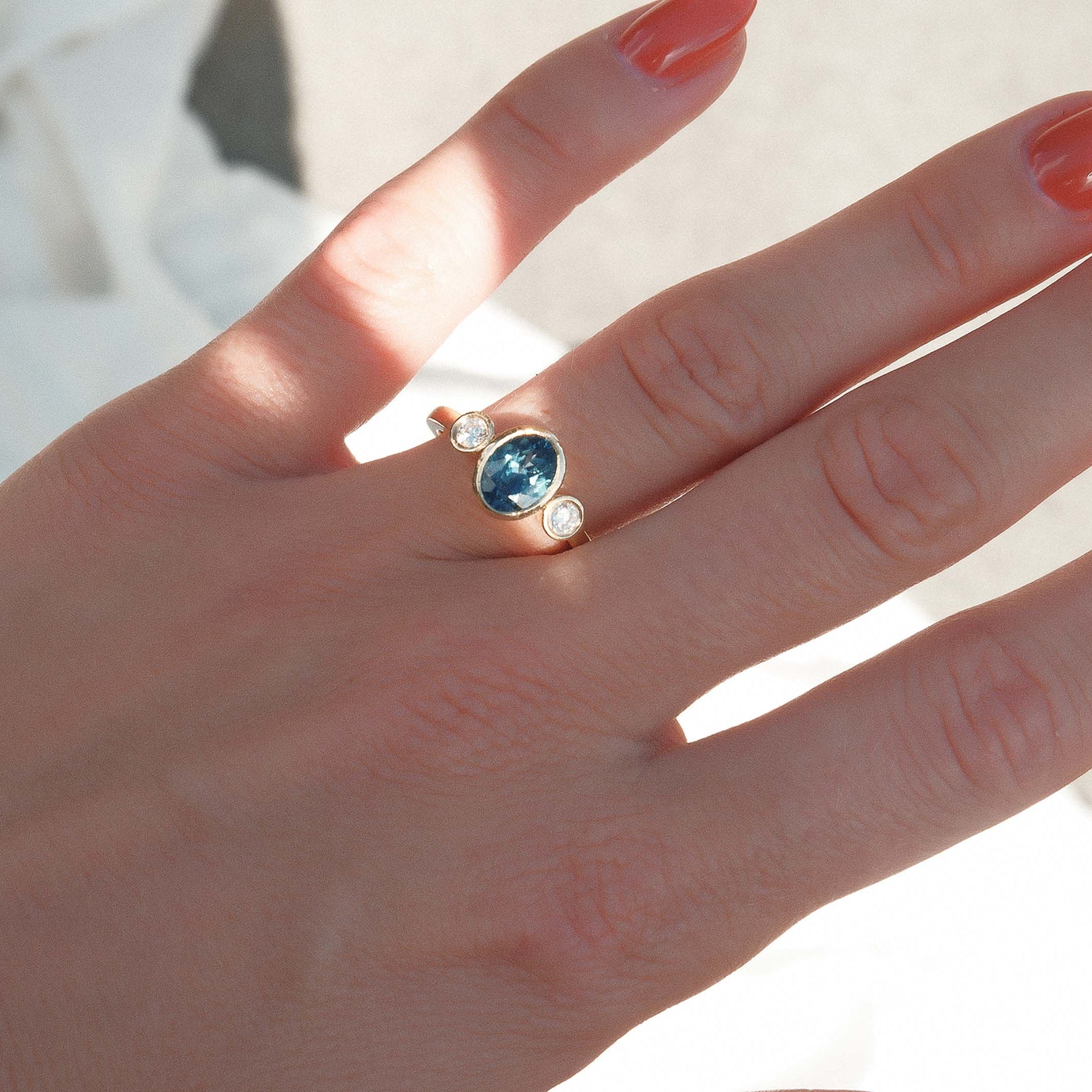 Hand wearing a ring with a blue gemstone on a light background