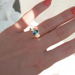 Hand wearing a ring with a blue gemstone on a light background