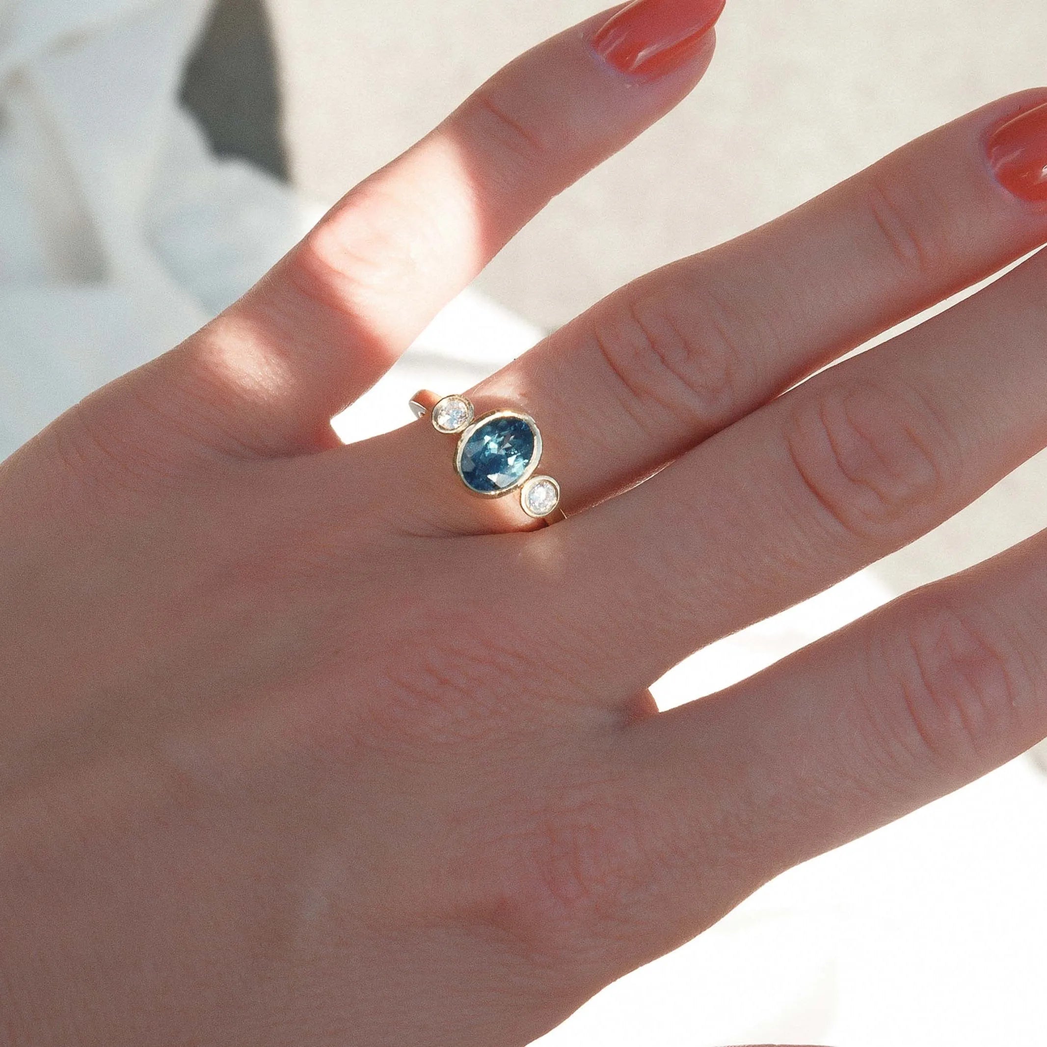 Hand wearing a ring with a blue gemstone on a light background