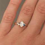 Close-up of a hand wearing a diamond ring with blue gemstones on a neutral background