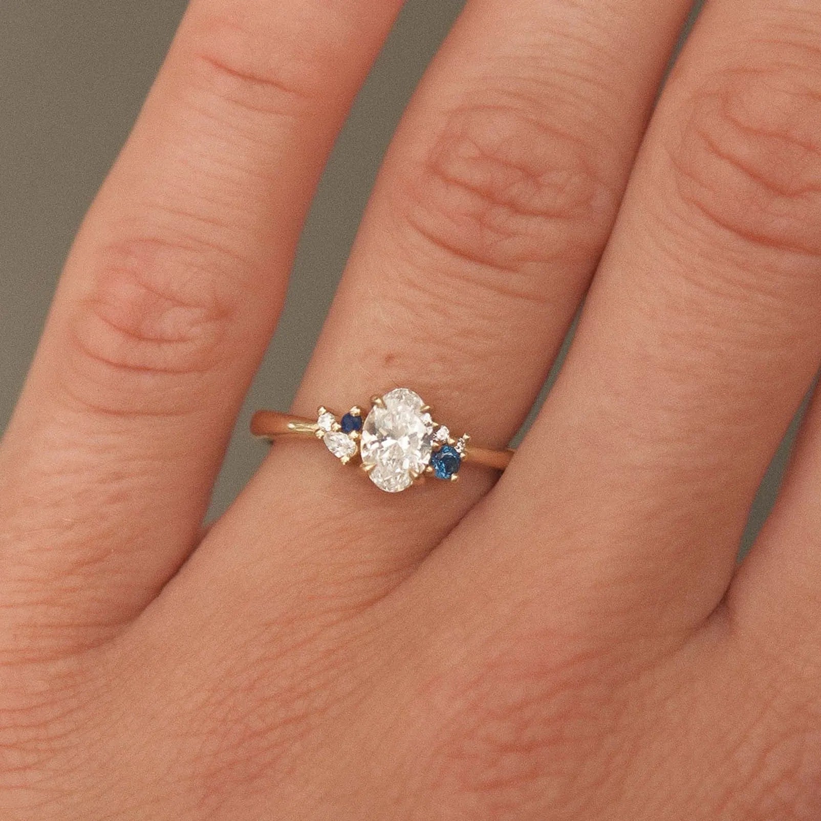 Close-up of a hand wearing a diamond ring with blue gemstones on a neutral background