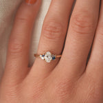 Close-up of a hand wearing an elegant ring with a diamond and blue gemstone on a neutral background.