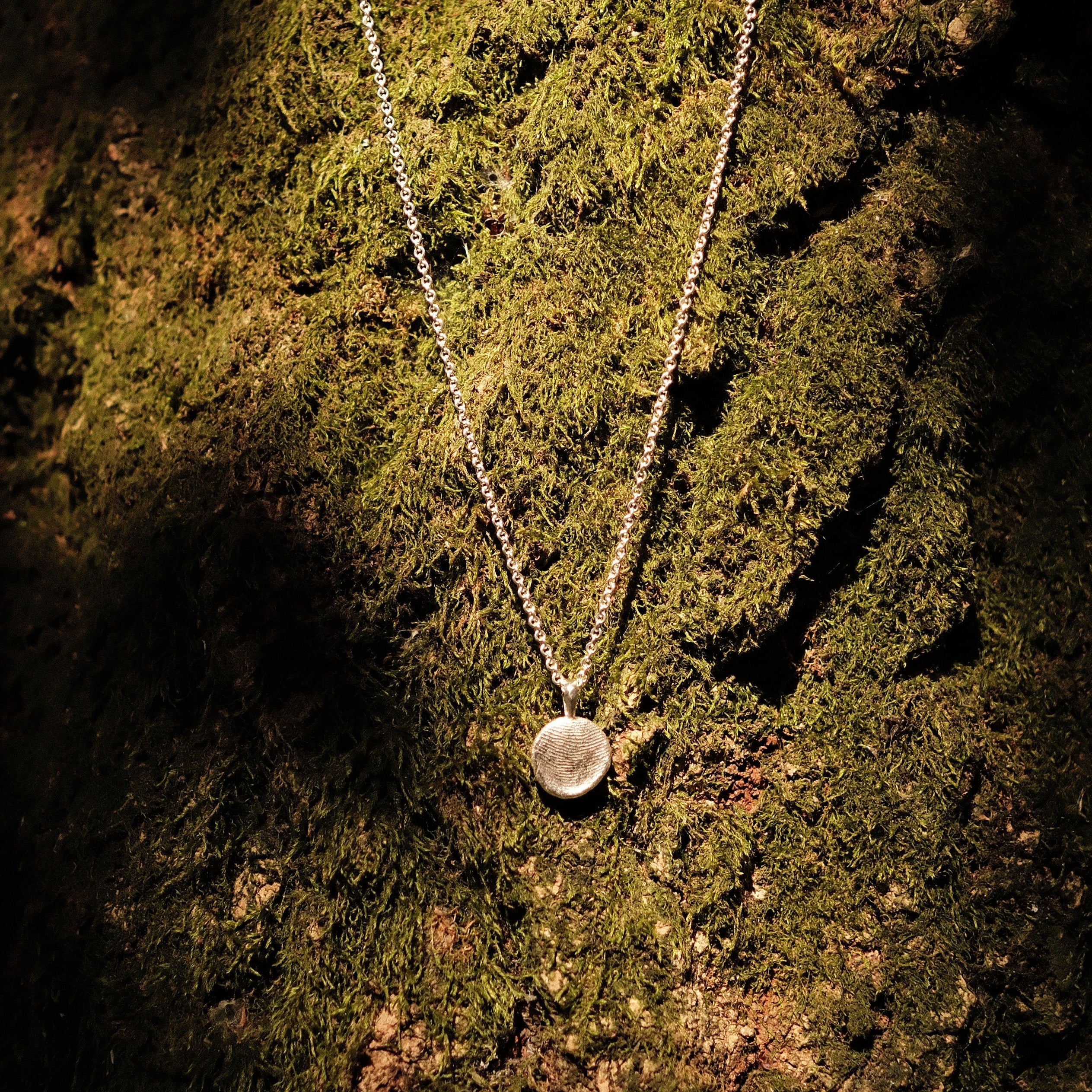 fingerprint pendant necklace infront of moss