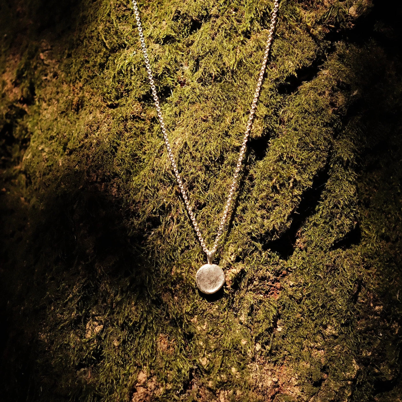 fingerprint pendant necklace infront of moss