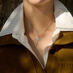 Person wearing a necklace with a dandelion-shaped pendant against a natural tree bark background