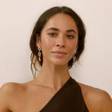 Woman wearing dangle star and moon earrings and a one-shoulder brown top against a plain background