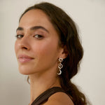 Woman wearing silver dangle star and moon earrings and a brown top with a neutral background