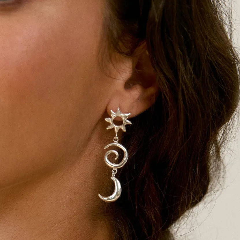 close up of ear wearing silver dangle earrings with sun, swirl and moon shapes