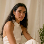 Woman in a white dress sitting against a beige curtain