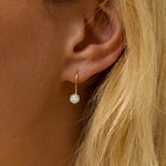 Close-up of an ear wearing a gold earring with a diamond, against a blurred background.