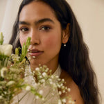 Woman holding flowers wearing diamond drop earrings with a neutral background